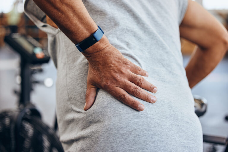Person mit Rückenschmerzen und Fitnessarmband